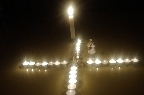 Keskellä kynttilä, jonka ympärillä tuikkuja, joista muodostuu risti. Vieressä Jeesus-hahmo.